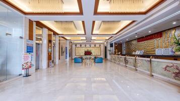A spacious lobby with a polished marble floor, a reception desk, and a seating area with blue sofas.