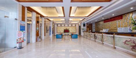 A spacious lobby with a polished marble floor, a reception desk, and a seating area with blue sofas.