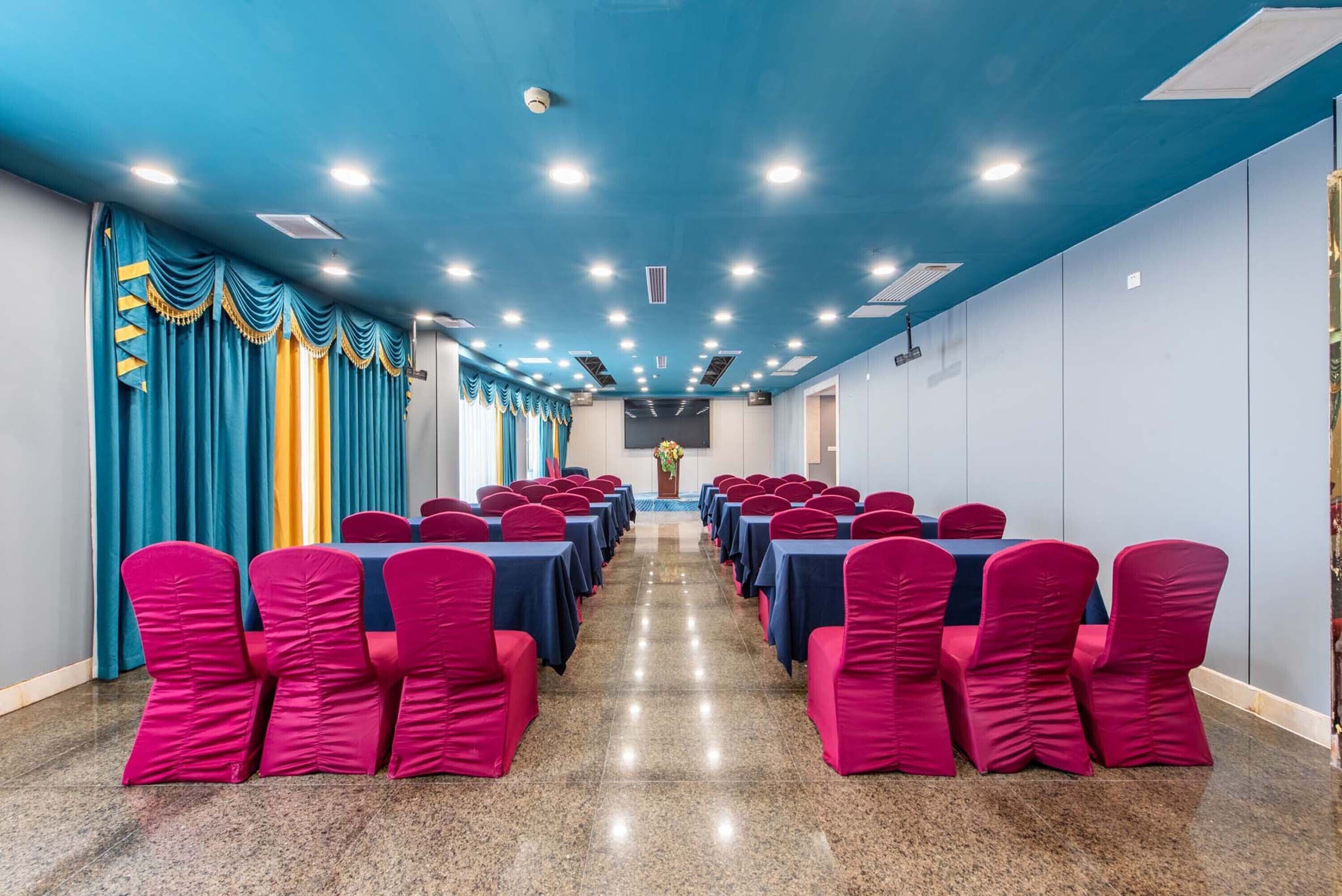 A conference room with rows of tables and chairs, blue curtains, and a polished floor.