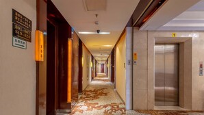 A hotel corridor with a patterned floor, an elevator, and directional signs on the walls. - Billions-Earn Hotel (Foshan)