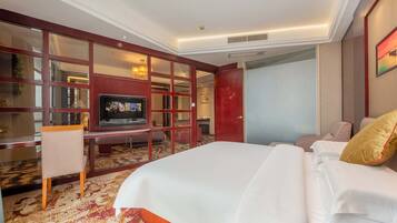 A hotel room with a large bed, a TV, a desk with a chair, and a bookshelf.