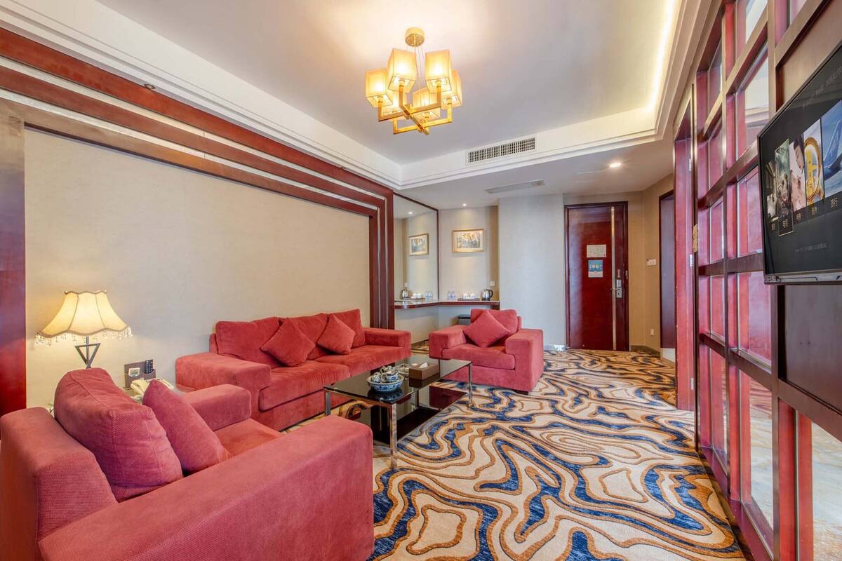 A hotel room with a red sofa set, a coffee table, a lamp, and a patterned carpet.