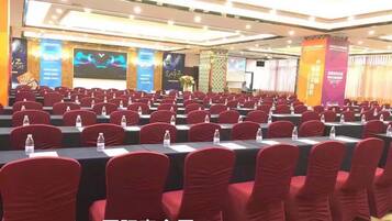 A conference room with rows of tables and chairs, banners, and a stage.
