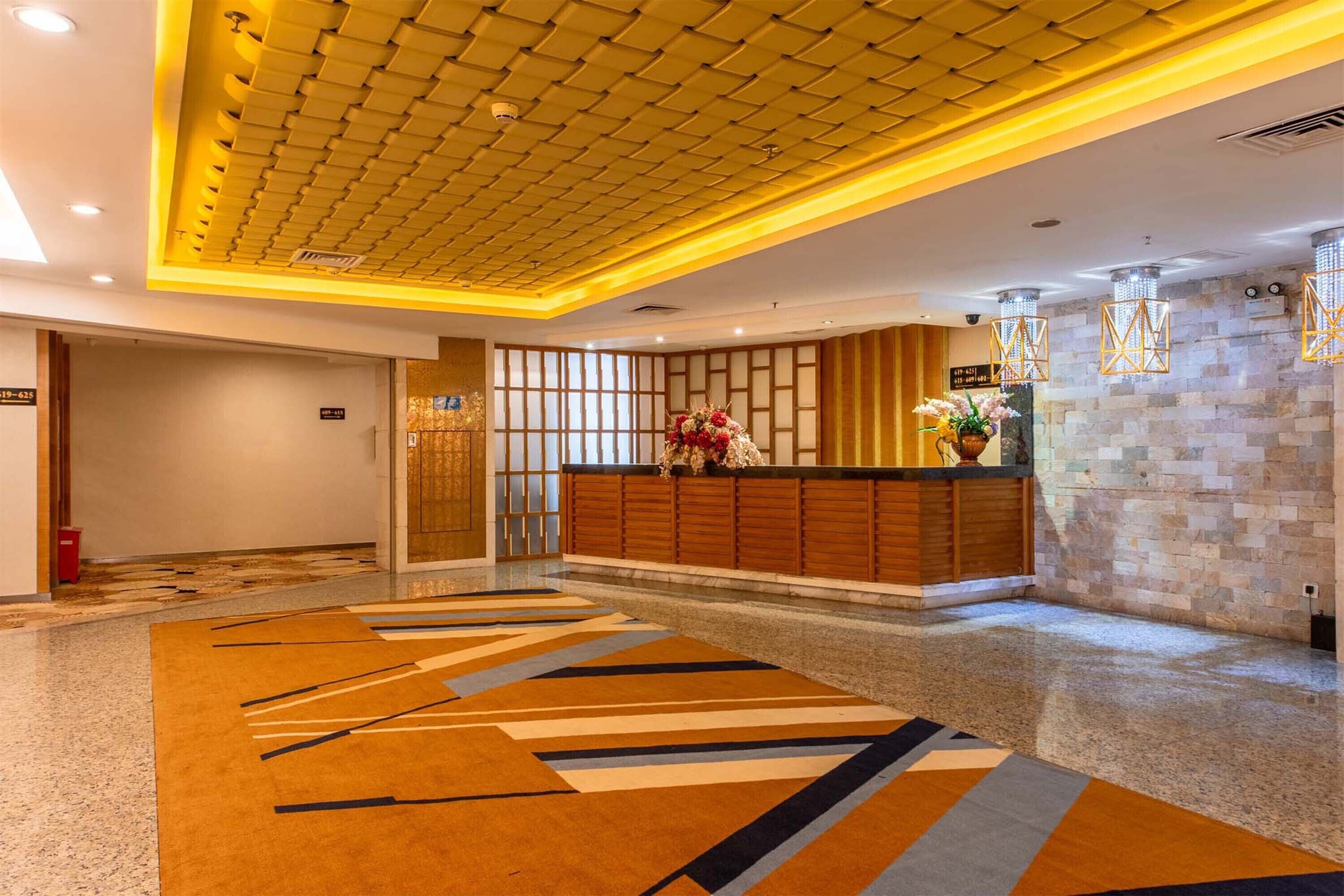 A hotel lobby with a reception desk, patterned carpet, and a stone wall with a clock.