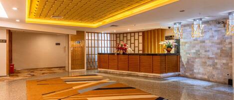 A hotel lobby with a reception desk, patterned carpet, and a stone wall with a clock.