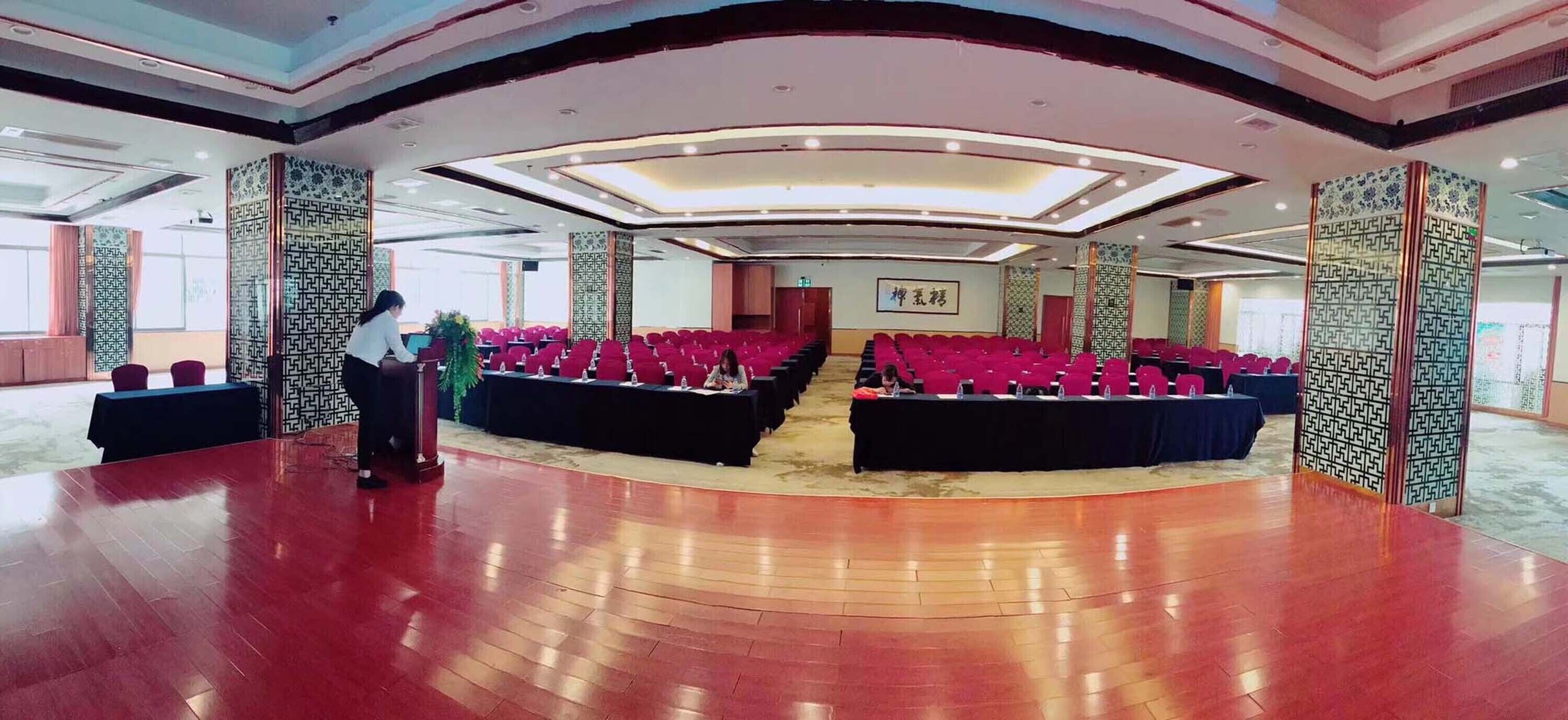 A conference room with rows of red chairs, a stage, and decorative panels.
