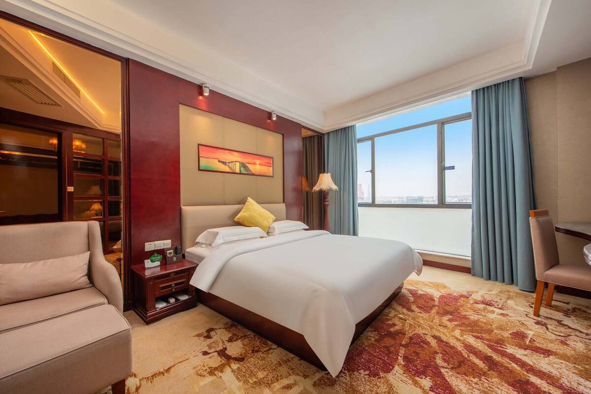 A hotel room with a large bed, a sofa, a desk, and a view of the city.