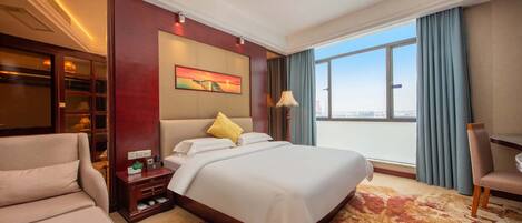 A hotel room with a large bed, a sofa, a desk, and a view of the city.