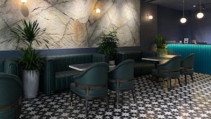 En restaurantindretning med stenvæg, grønne siddepladser og et mønstret gulv.