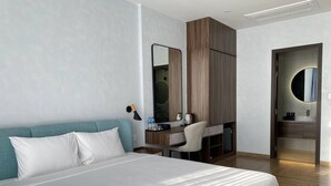 Et moderne hotelværelse med en stor seng, et skrivebord, en stol, et spejl og et badeværelse med et rundt spejl.