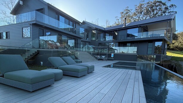 Ein modernes, zweistöckiges Haus mit einer Holzterrasse und einem Swimmingpool.