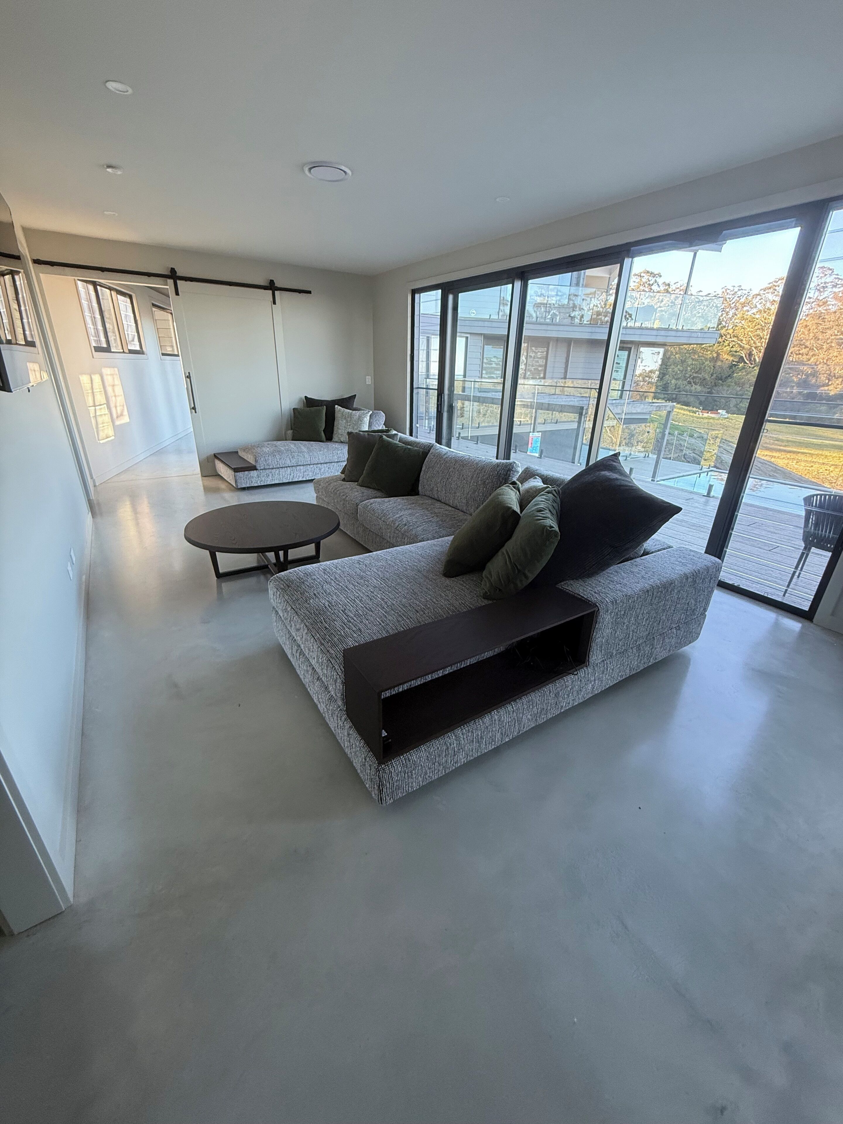Un salon moderne avec un canapé gris, une table basse et une grande fenêtre donnant sur l’extérieur.