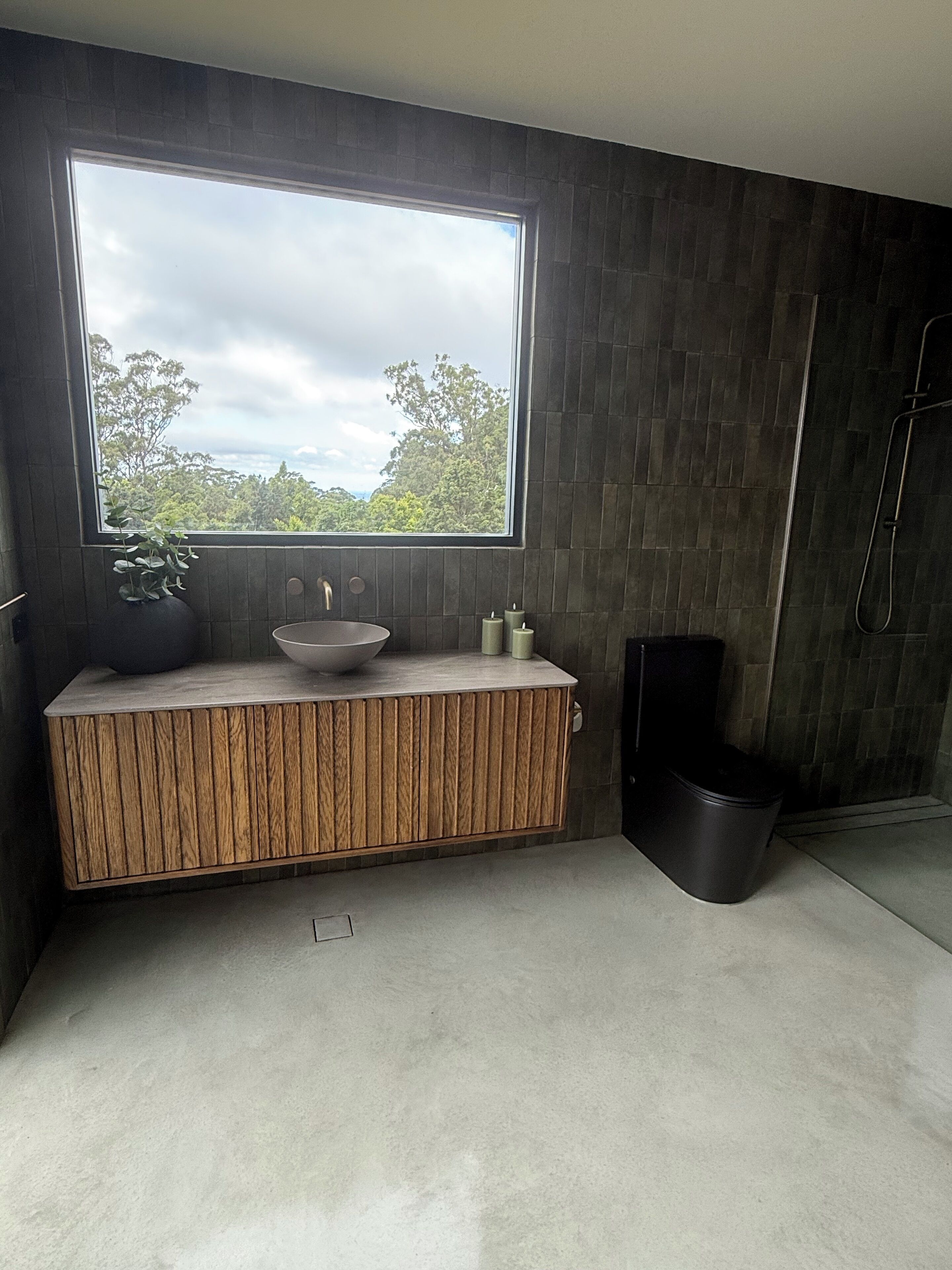 A modern bathroom with a large window, a wooden vanity, a sink, and a shower area.