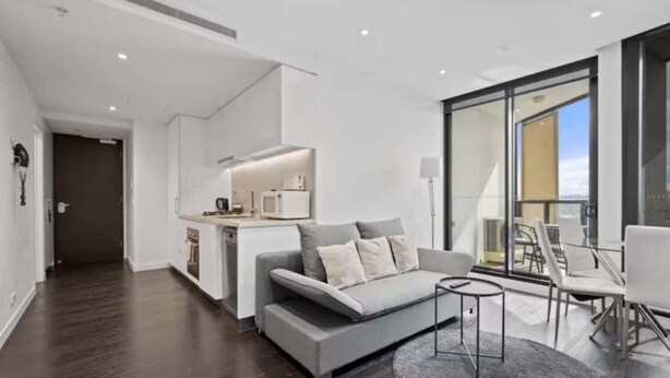 Ein modernes Wohnzimmer mit einem grauen Sofa, einem kleinen Couchtisch und einem Essbereich mit Stühlen.