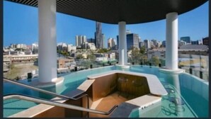 Ein Dachpool mit unendlicher Optik und Blick auf die Stadt, gestützt von weißen Säulen, sowie ein gläserner Bereich mit Sitzgelegenheiten.