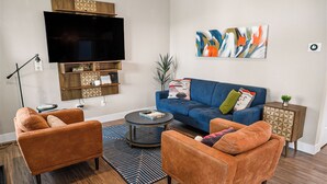 Een woonkamer met twee oranje banken, een blauwe bank, een flatscreen televisie, een boekenkast en een potplant.