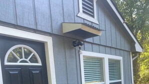 A house with a black front door, a covered porch with two chairs and a table, and a window with shutters. - Casa Hornitos/Beautiful Cottage 8 min from lake (Livingston)