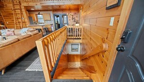 Un interior de madera con una escalera que sube a un segundo piso, un sofá y una zona de cocina.