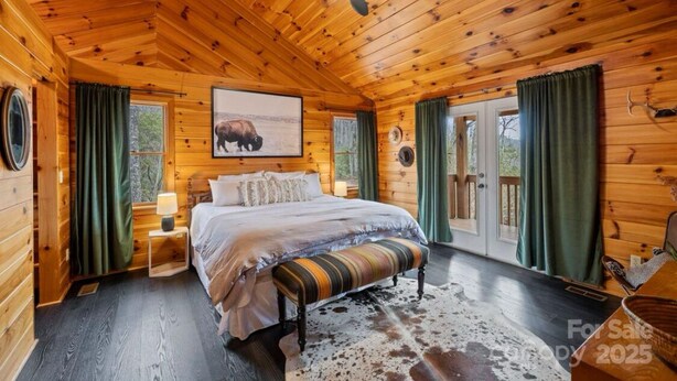 Une chambre située dans un chalet en rondins, avec un grand lit, un ventilateur de plafond et une fenêtre avec des rideaux.