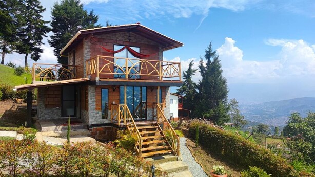 Ein zweistöckiges Haus mit Balkon, umgeben von Grün und Blick auf die Landschaft.