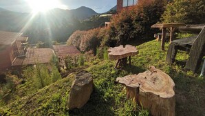 Ein modernes Gebäude mit Backsteinfassade und großen Fenstern, umgeben von einem Garten mit Holztischen und einer rustikalen Holzbank.
