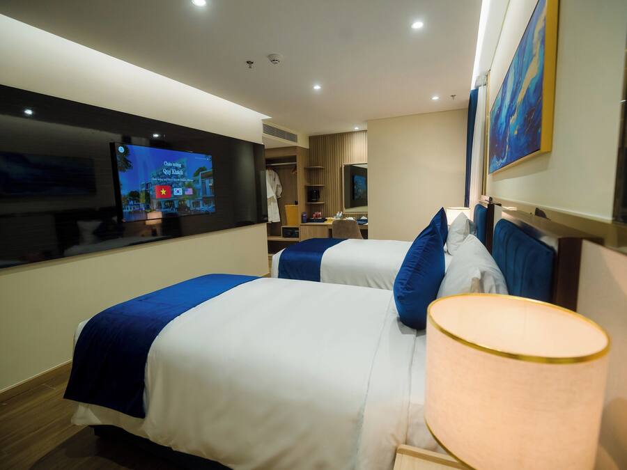 A hotel room with two beds, a TV, a desk, and a large painting.