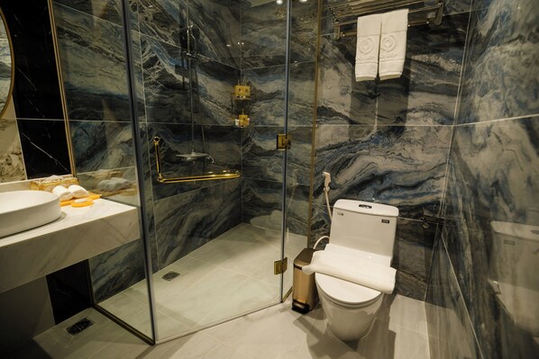 A modern bathroom with a glass-enclosed shower, a white sink, and marble walls. - Sandals Mimosa (Xuan Huong - Da Lat)