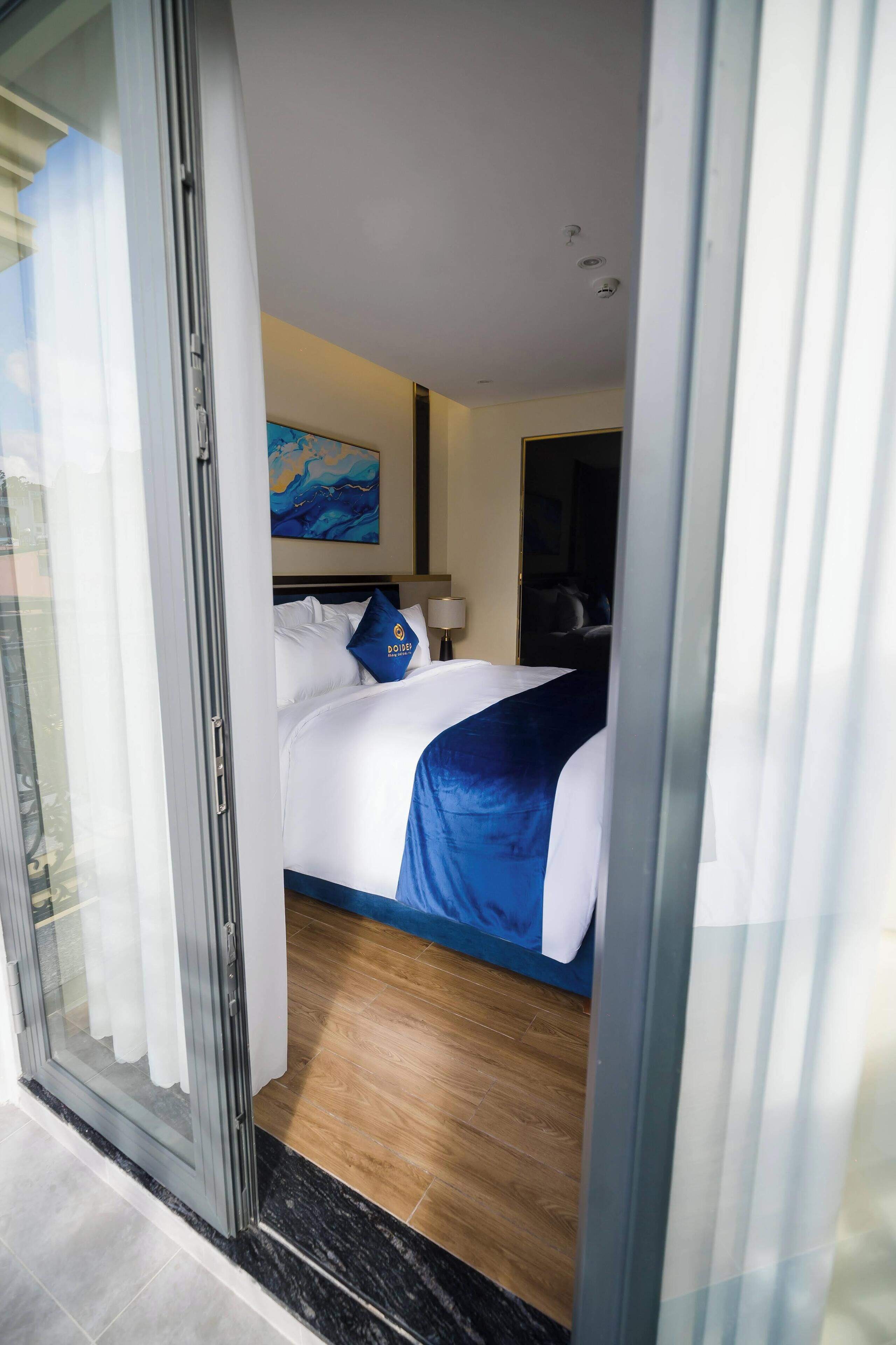 A hotel room with a bed, a painting on the wall, and a door leading to another room.