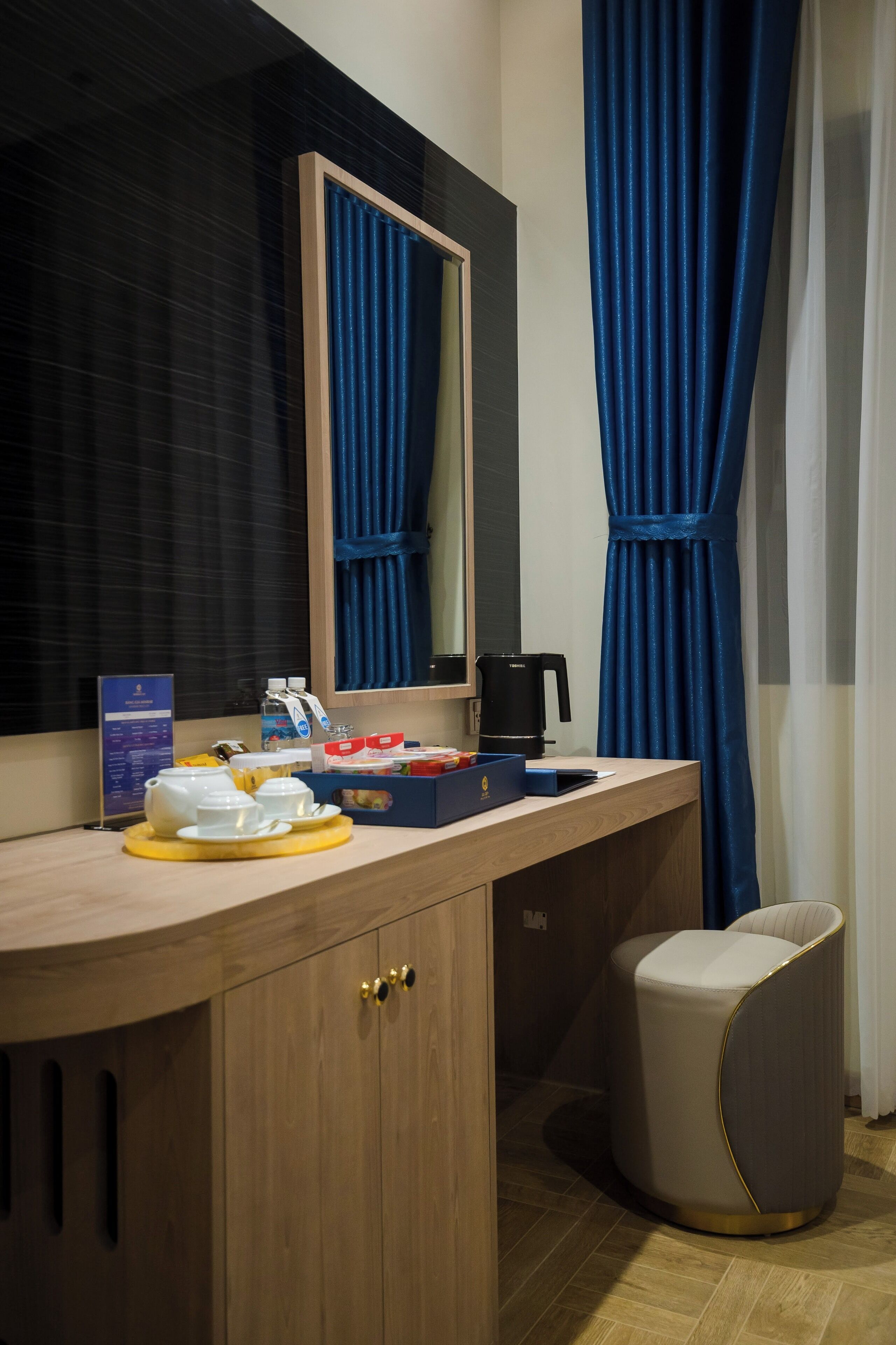 A hotel room with a wooden vanity, a mirror, a coffee maker, and a small seating area.