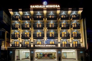 Um hotel com vários andares, varandas, uma placa de destaque e uma entrada bem iluminada.