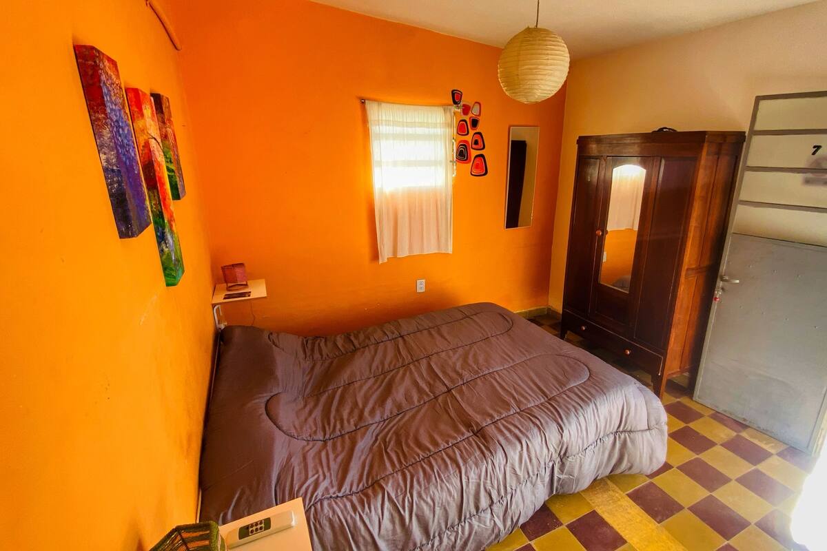 Ett rum med orangefärgade väggar, en säng, en garderob och ett fönster med gardiner.