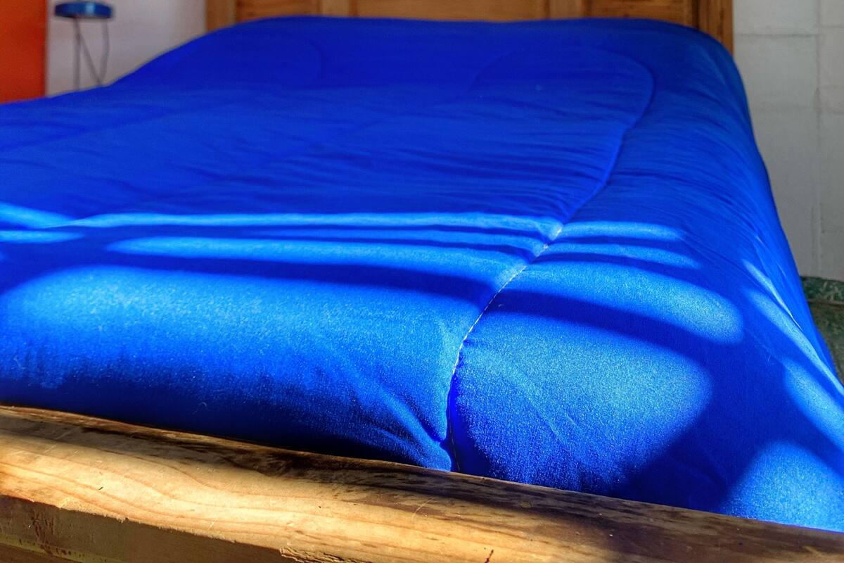 En säng med en träram som huvudgavel och ett blått överkast.