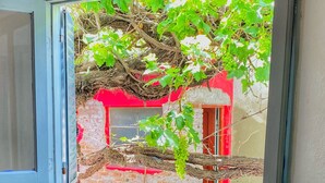 A window with a view of a brick wall and a red door. - Hostal de Luz (Capilla del Monte)