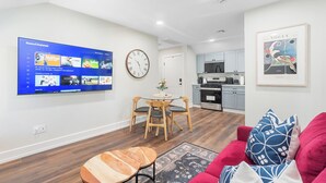 A modern living room with a flat-screen TV, wooden dining table, and red sofa.