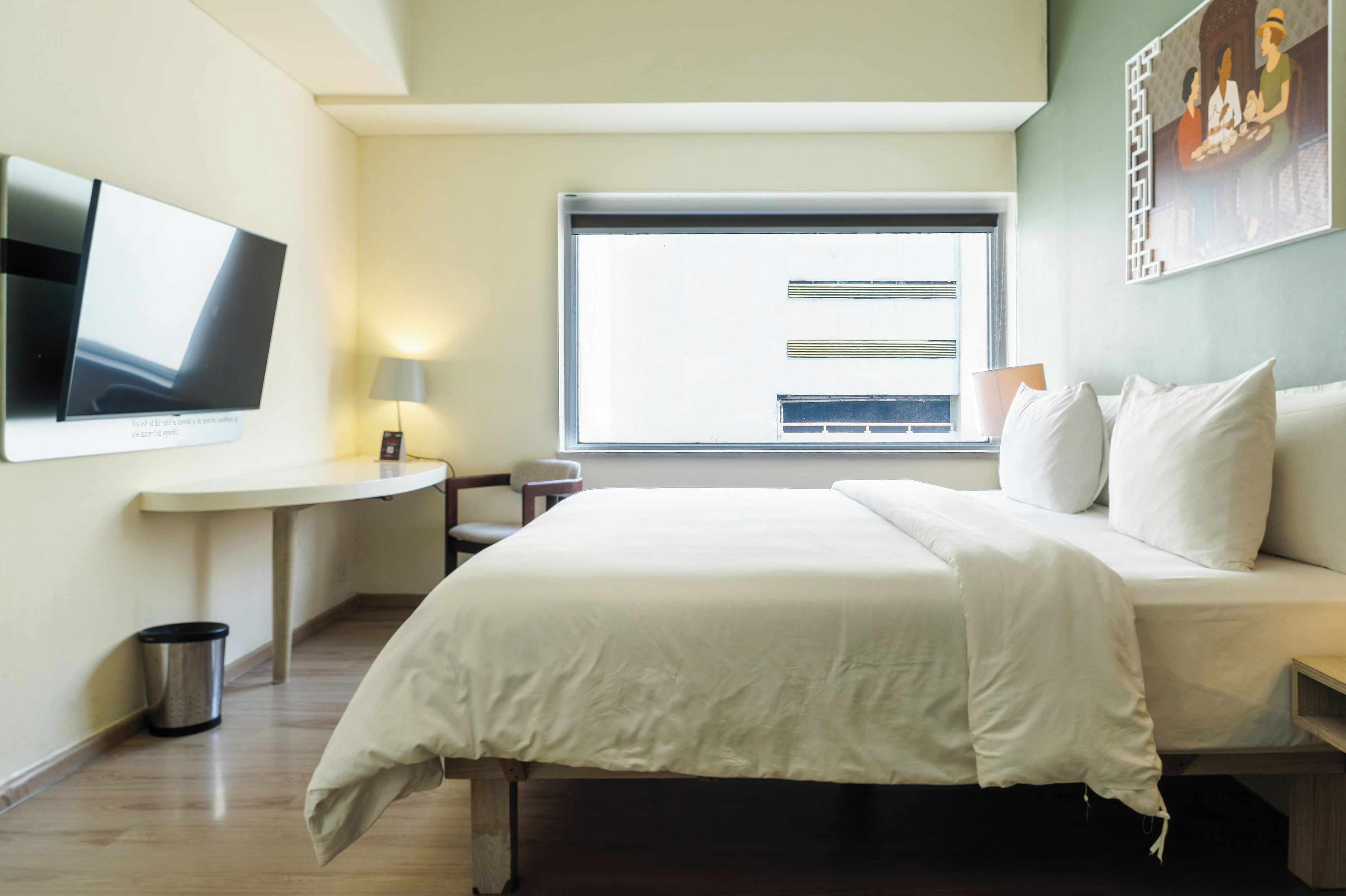 A hotel room with a bed, a desk, a chair, a TV, a window, and a trash bin.