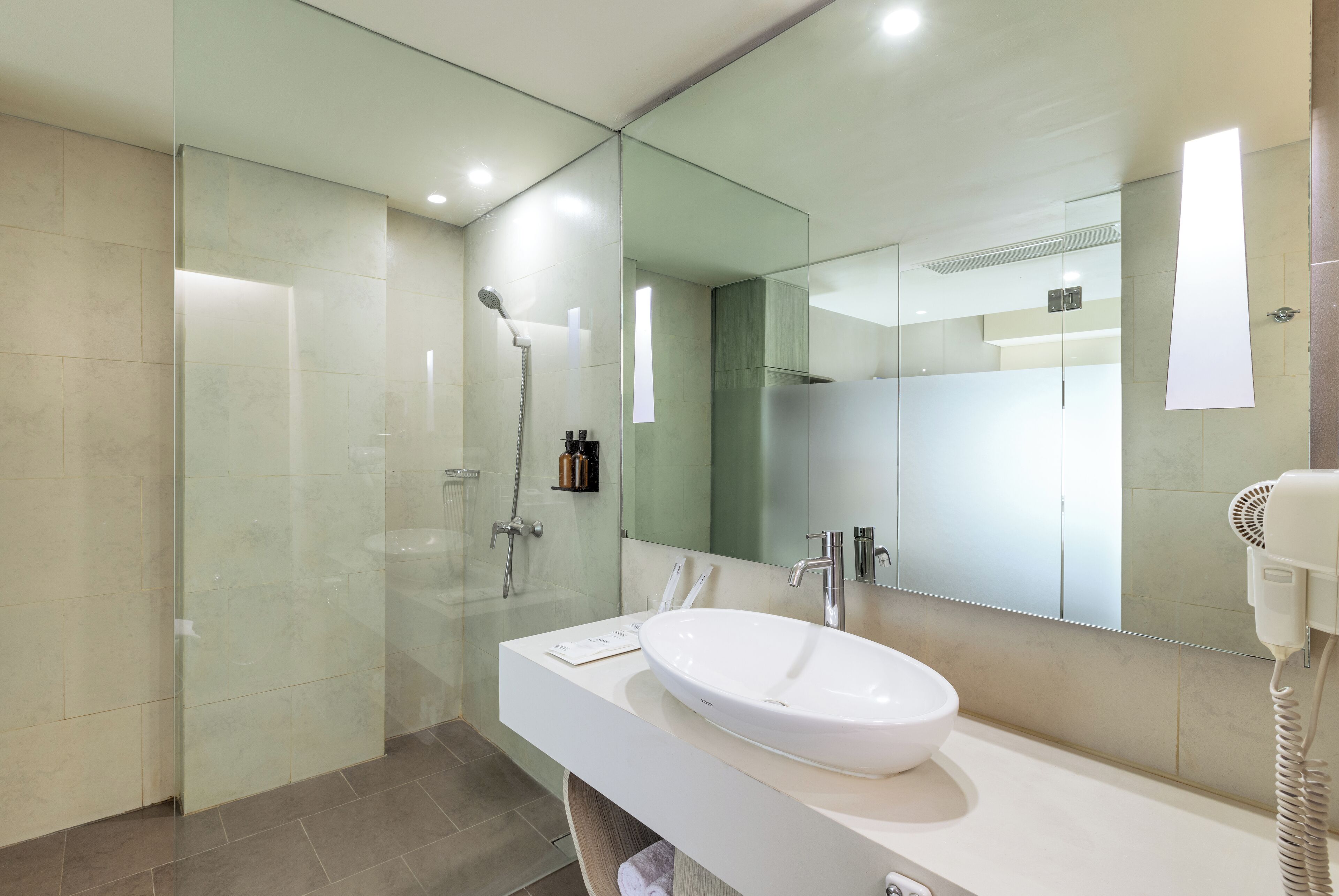 A modern bathroom with a glass-enclosed shower, a white sink, and a large mirror.