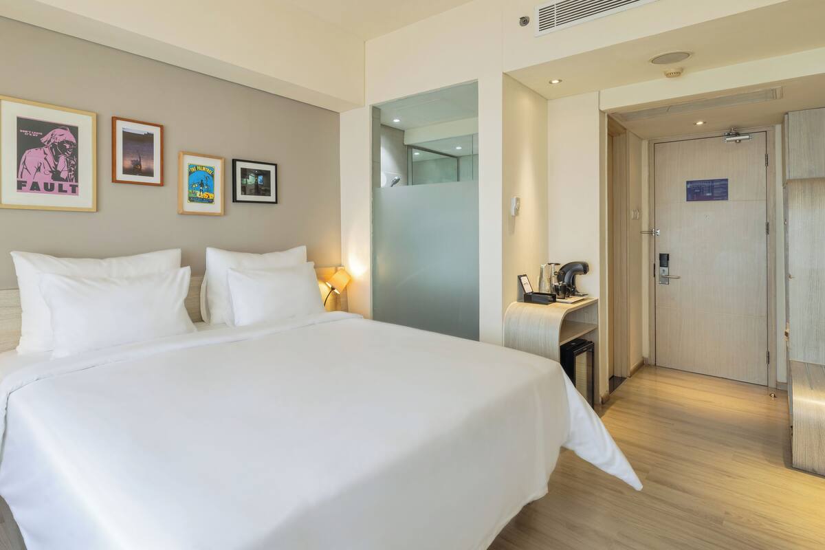 A hotel room with a large bed, a desk with a coffee maker, and framed pictures on the wall.