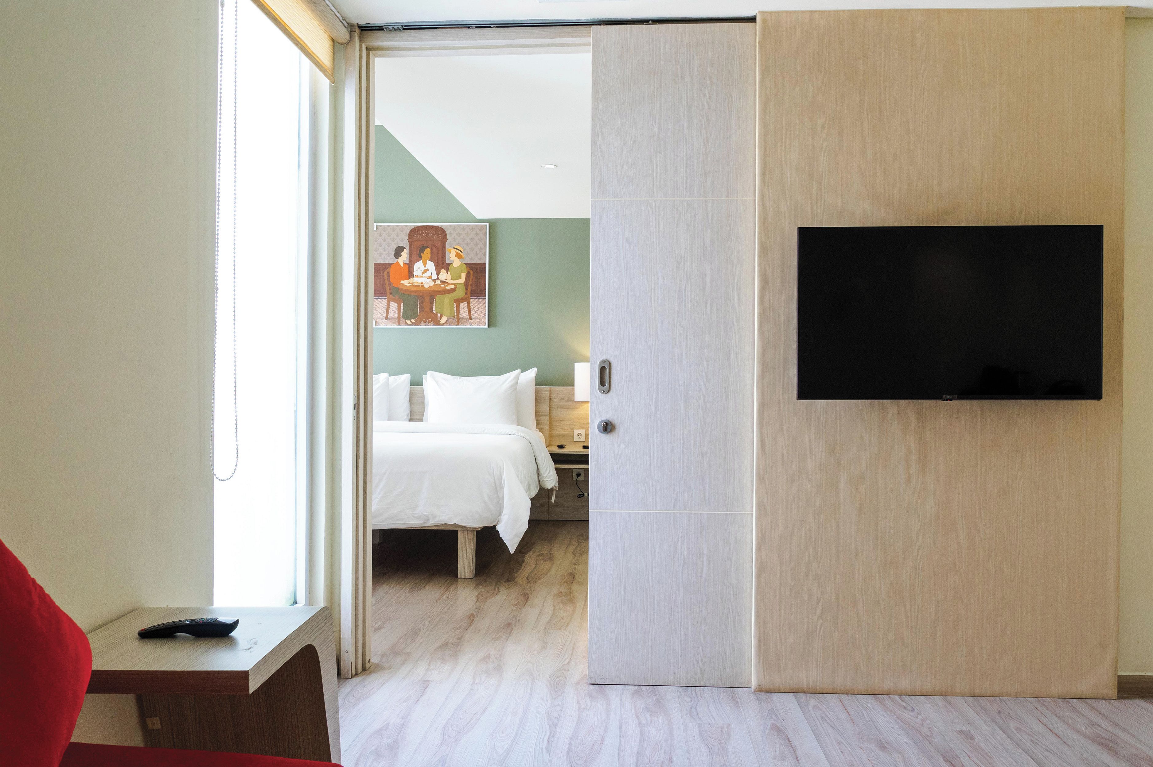 Une chambre d’hôtel avec un lit, un téléviseur fixé au mur et une fenêtre avec des rideaux.