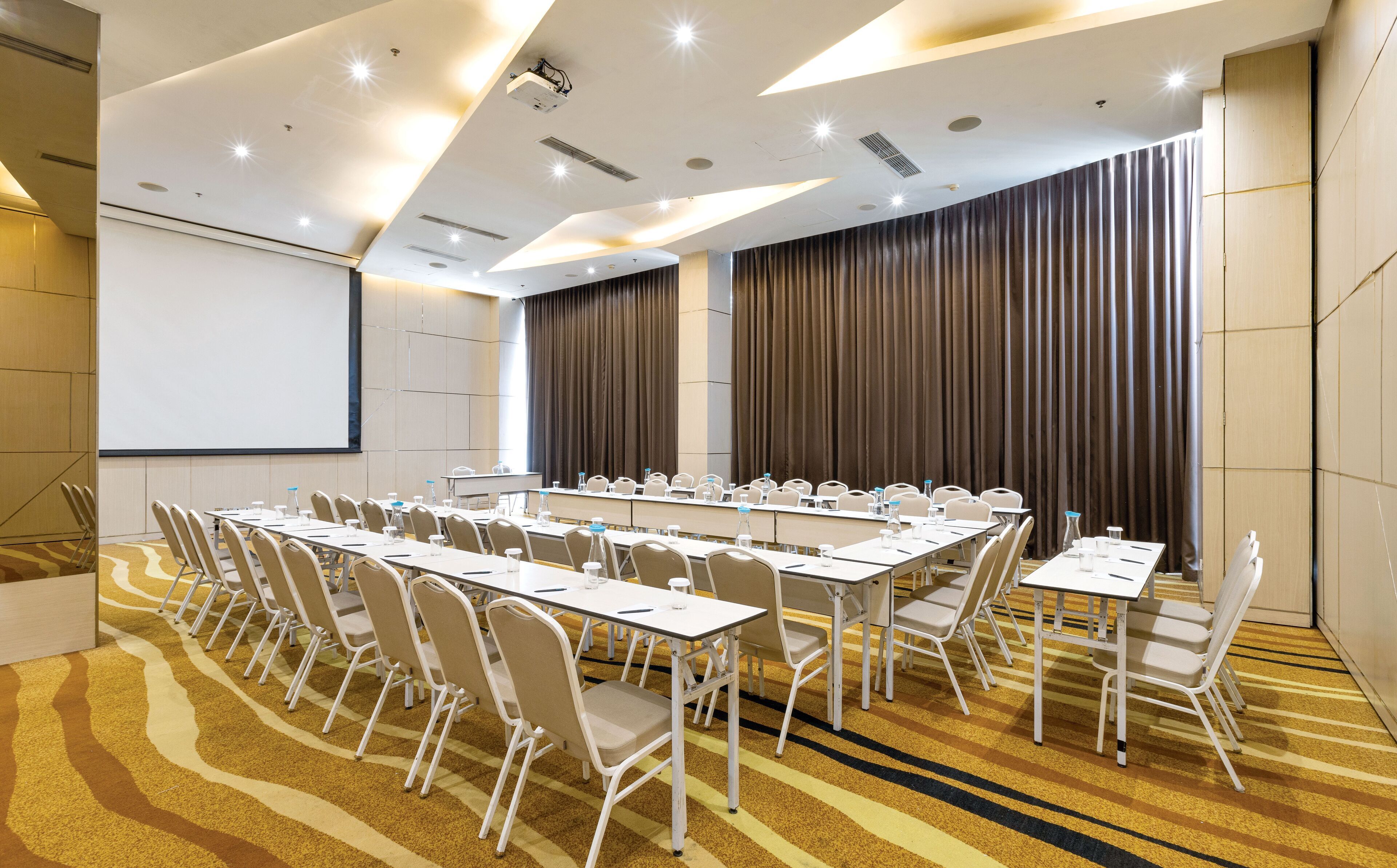 A conference room with a long table, chairs, a projector screen, and a large window with curtains.