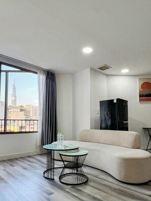 A modern living room with a curved sofa, a round glass table, and a view of a cityscape through large windows. - Zeus Living - 7C Downtown By Feet (Ho Chi Minh City)