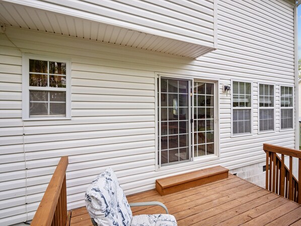 A wooden deck with a bench and a chair, a sliding glass door, and white siding on a house.