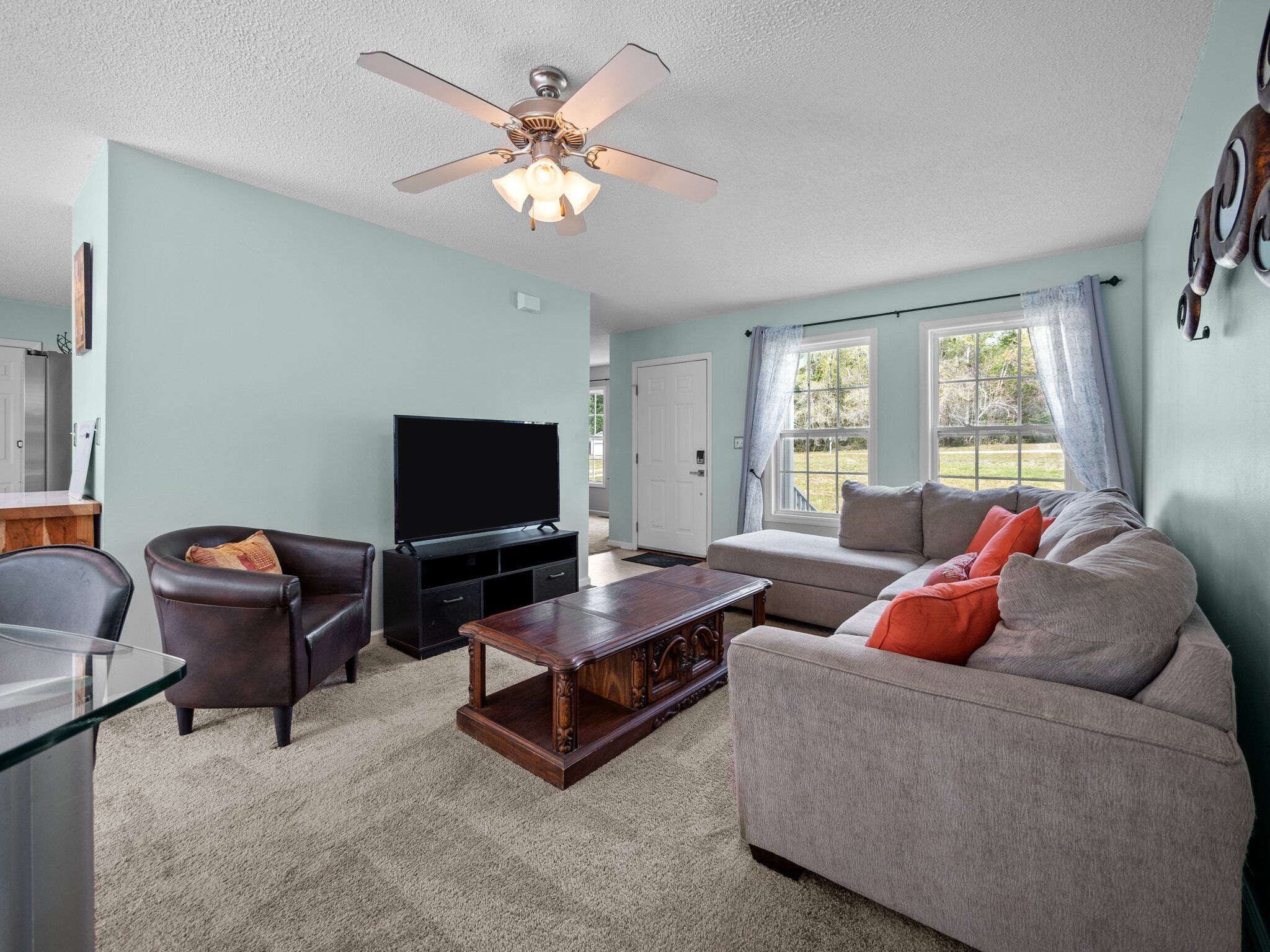 A living room with a flat-screen TV, leather chairs, a wooden coffee table, and a grey sofa with orange cushions.