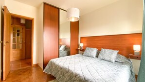 Camera da letto con un letto grande, una testiera in legno, lampade sui comodini, uno specchio e una porta che dà su un'altra stanza.