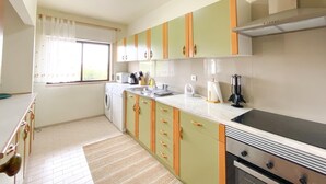 Una cucina compatta con mobili verdi e beige, un forno a microonde integrato e un piano cottura.