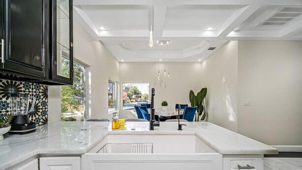 A modern kitchen with white cabinetry, a large island with a sink, and a view to the outside. - Sprawling Home w/ Rooftop Spot (San Antonio)