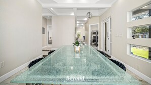 A spacious, modern interior with a long, glass-top table and a view of a green lawn through a window. - Sprawling Home w/ Rooftop Spot (San Antonio)