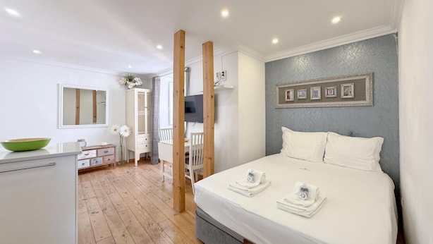 A bedroom with a bed, a dresser, a vanity, a mirror, a TV, and a wall with framed pictures. - Comfort in the heart of Alfama (Lisboa)
