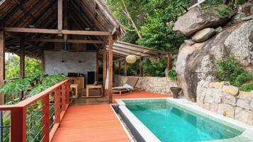 Um deck de madeira com piscina, cadeiras de descanso e uma parede de pedra.