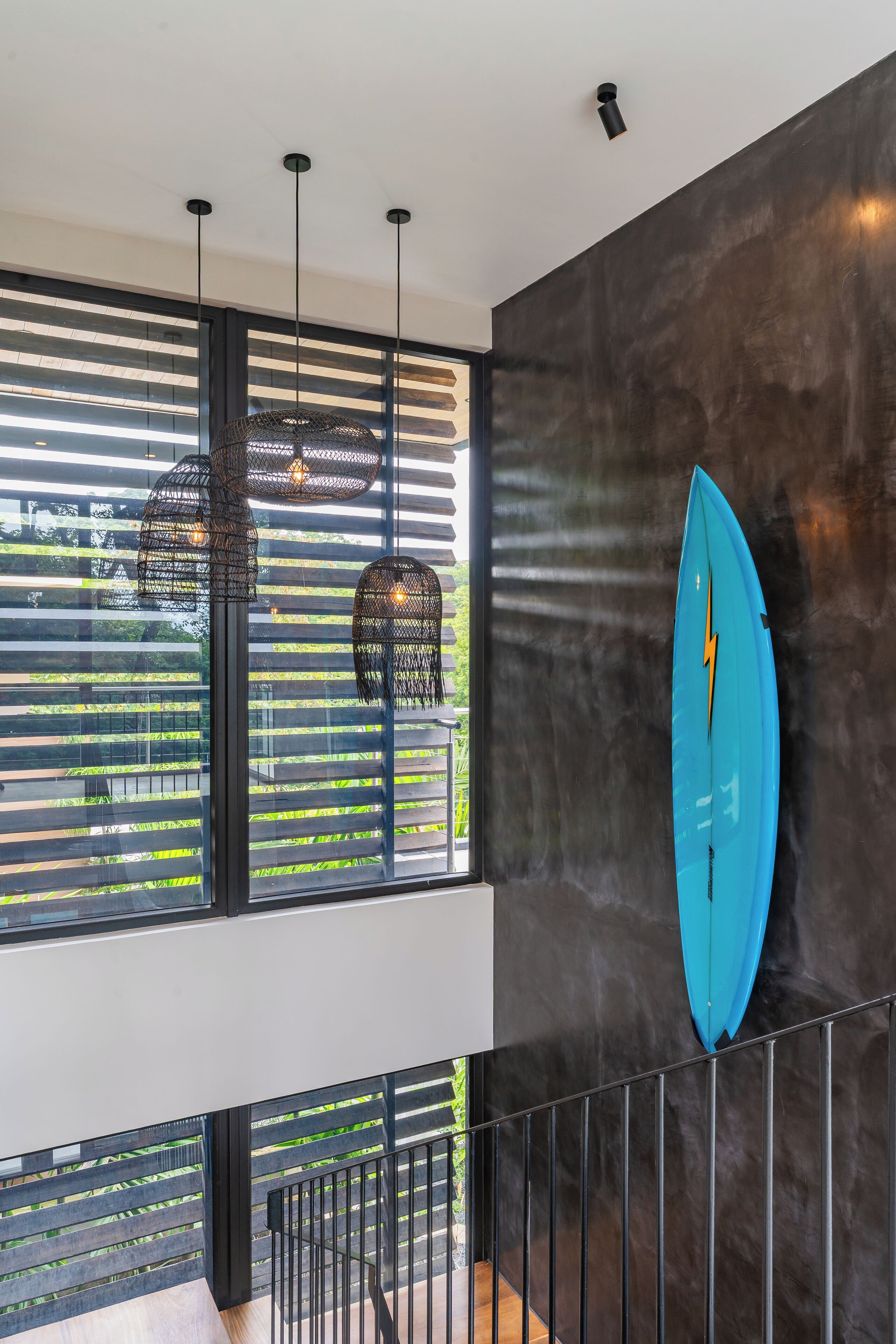 A modern interior with a large window, black metal railings, and a blue surfboard mounted on the wall.