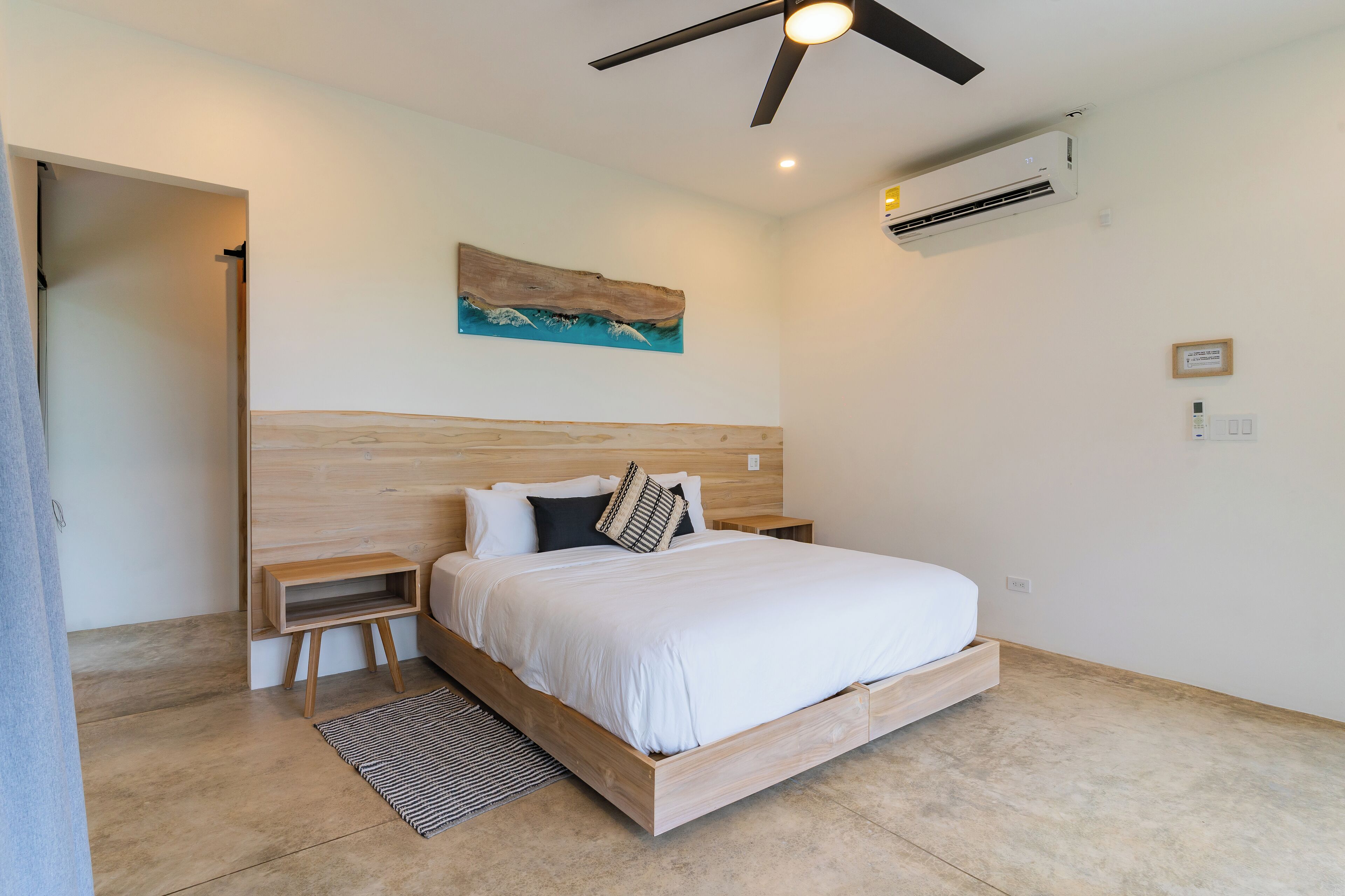 Een moderne slaapkamer met een houten bed, een plafondventilator, een airconditioner en een schilderij aan de muur.